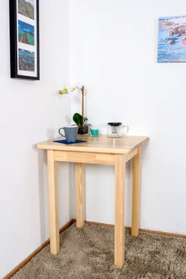 A small wooden table in a corner with a mug and a coffee maker on it.