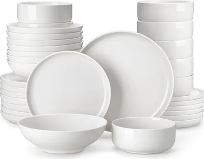 A collection of white ceramic dishes, including plates and bowls, stacked and arranged on a white background.