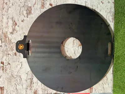 A round metal plate with a hole in the center, resting on a textured surface next to green artificial grass.