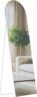 A full-length mirror with a white frame, reflecting a living room scene with a sofa, a plant, and curtains.