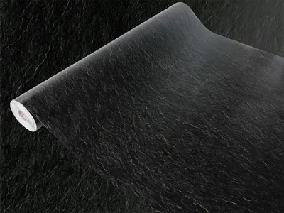 A roll of black slate-effect wallpaper is shown with the edge unrolled, lying on a black textured surface.