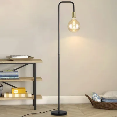 A floor lamp with a vintage design is placed next to a shelf unit filled with books and decorative items, in a room with wooden flooring and light-colored walls.