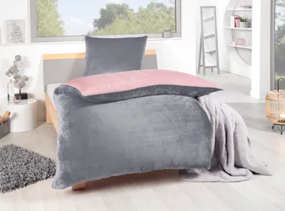 A bed with grey and pink bedding in a bedroom setting.