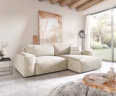 A modern living room with a large sectional sofa, abstract art, and a large window overlooking a garden.