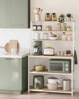 A modern kitchen scene with a white tiled backsplash, sage green cabinets, and a white shelving unit filled with kitchen appliances and decor.