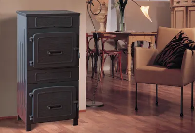 A dark gray cast iron stove is shown in a living room setting with a wooden table and chairs in the background.