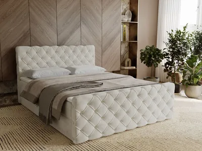A bedroom scene with a tufted boxspring bed as the focal point, decorated with pillows and a throw blanket. The background features a wooden wall paneling and a bookshelf with decorative items and plants.