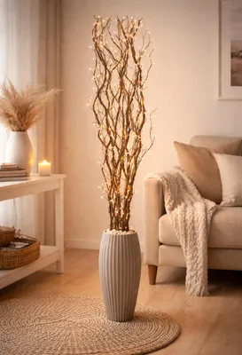 A decorative branch with lights in a vase, placed in a living room setting next to a sofa and a side table.