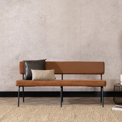 A brown leather bench with two pillows against a textured wall.