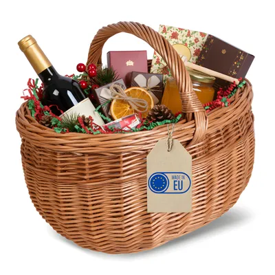 A wicker picnic basket filled with festive items, including a bottle of wine, chocolates, dried oranges, pinecones, and a jar of honey.