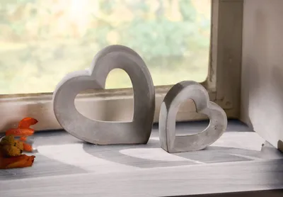 Two heart-shaped concrete decorations sit on a windowsill with autumn leaves and a cookie nearby.