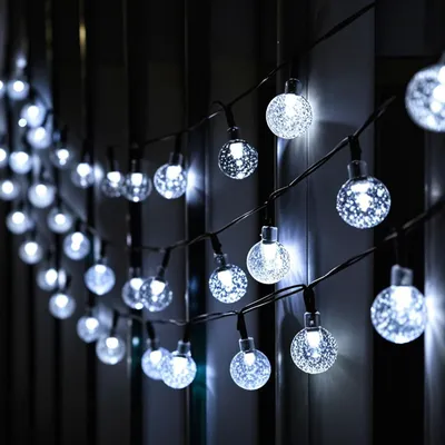 A string of solar-powered globe lights with a textured, frosted appearance, hanging outdoors at night against a dark background.