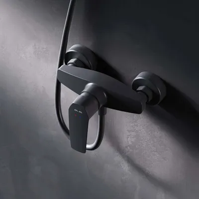A close-up shot of a black shower faucet mounted on a dark gray textured wall.