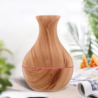 A wooden-patterned humidifier is placed on a table with some greenery and folded fabric in the background.