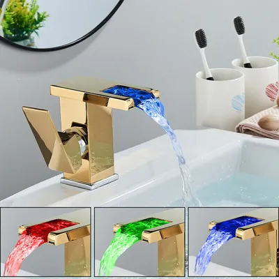 A gold LED waterfall faucet with blue, red, and green water flow, shown in a bathroom sink setting with toothbrushes and a mirror in the background.