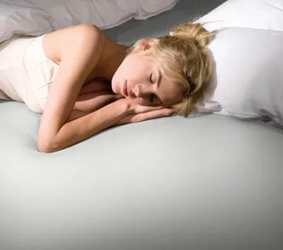 A woman sleeping in a bed with white bedding.