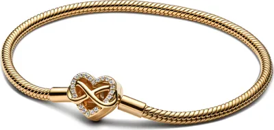 A gold-colored bracelet with a heart-shaped charm featuring an infinity symbol and small clear stones, presented on a white background.