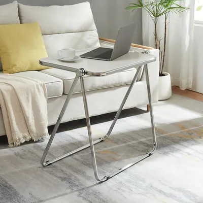 A folding side table with a laptop and a cup of coffee on it, placed next to a sofa in a living room.