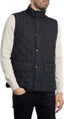 A man wearing a dark blue quilted vest over a cream-colored sweater.