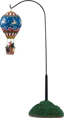 A decorative hot air balloon ornament with a Christmas theme, suspended from a black stand with a green, grassy base.