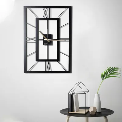 A modern black metal wall clock with Roman numerals is displayed on a white wall.