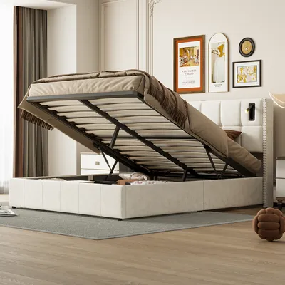 A bedroom scene with a bed frame open, revealing storage space underneath. The bed is upholstered in beige fabric and has a tufted headboard. There are framed pictures on the wall behind the bed.