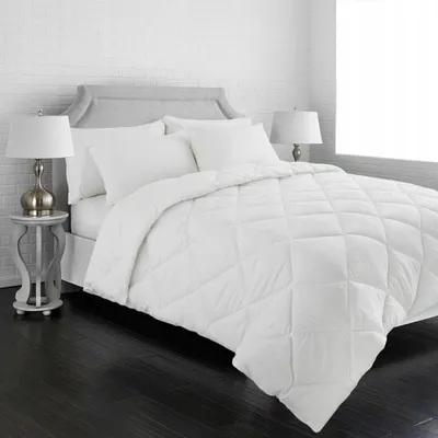 A white comforter is laid out on a bed with pillows and a headboard.