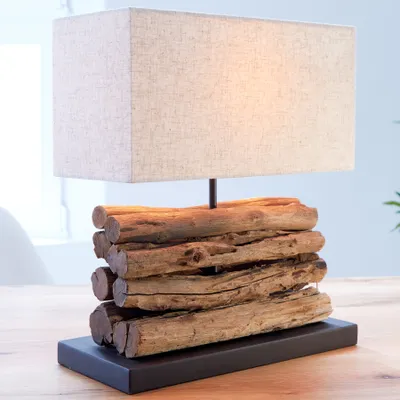 A table lamp with a driftwood base and a beige linen shade sits on a wooden table.