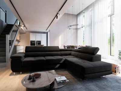 A modern living room with a large black sectional sofa, coffee table, and stairs leading to an upper level. Large windows with sheer curtains are visible in the background.