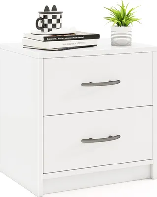 A white nightstand with two drawers is shown against a white background. There are books and a plant on top of the nightstand.