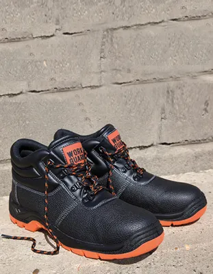 A pair of black work boots with orange accents are placed on a concrete surface in front of a brick wall.