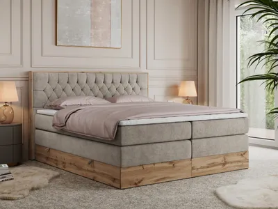 A bedroom scene with a large bed as the focal point, decorated with bedding and a headboard. A bedside table with a lamp and a plant are also visible.