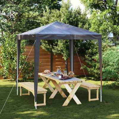 A party tent set up in a garden with a picnic table and benches.
