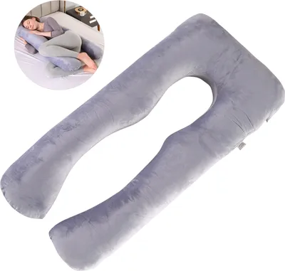 A woman is lying on a bed using a U-shaped pregnancy pillow.