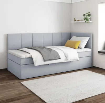 A light blue upholstered bed with white and gray bedding, set against a white wall and wooden floor.