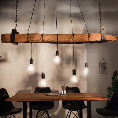 A rustic wooden beam chandelier with five exposed bulbs hangs above a wooden dining table with black chairs.