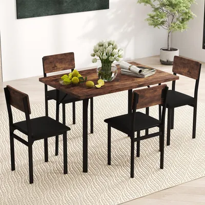 A dining set with a wooden table and four black chairs is placed on a rug in a room with a plant and a painting on the wall.
