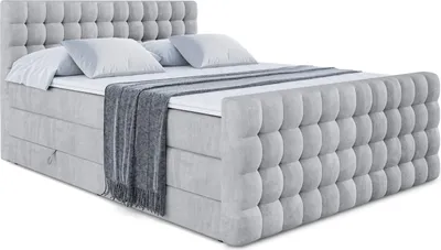 A light gray upholstered boxspring bed with a tufted headboard and footboard, made up with white bedding and a gray throw blanket.