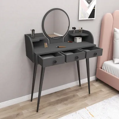 A dark gray vanity table with a round mirror and three drawers, set against a light gray wall with a pink headboard visible to the right.