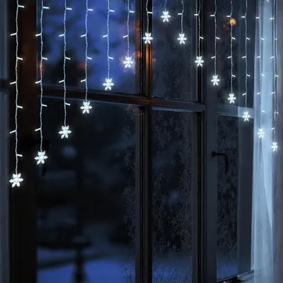 Snowflake string lights hanging on a window at night.