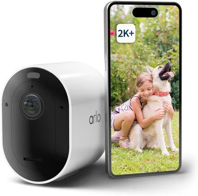 A white Arlo Pro 5 2K spotlight security camera is shown next to a smartphone displaying a live feed of a girl hugging a dog.