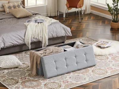 A bedroom scene with a bed, a storage ottoman, and a rug.