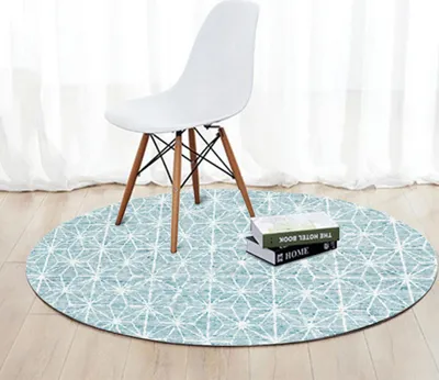 A white chair is placed on a round rug with a geometric pattern, in front of a window with white curtains.