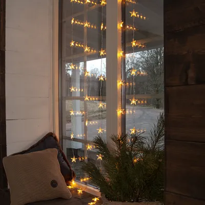 A window sill decorated with star-shaped string lights, a pillow, and a pine branch.