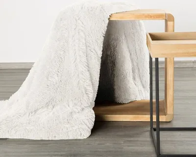 A fluffy white blanket draped over a wooden side table.