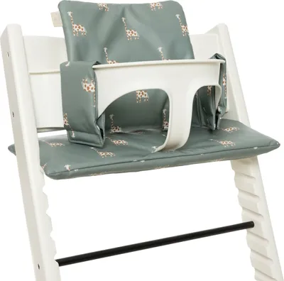 A close-up view of a white high chair with green giraffe-patterned seat and back cushions.