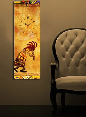 A tall, narrow clock with an indigenous-inspired design is mounted on a wall next to a tufted armchair.