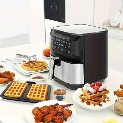 An air fryer is shown on a table with various food items, including waffles, fried chicken, and fruit.