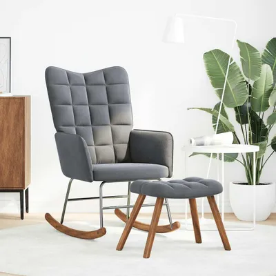 A grey rocking chair and ottoman are shown in a well-lit room with a large plant and a side table.
