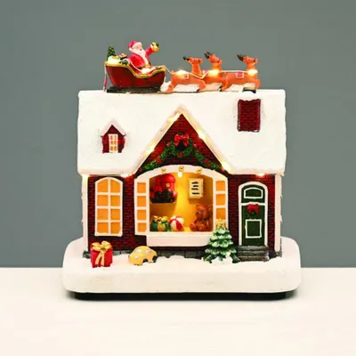 Immagine prodotto di ACA Decorazione natalizia illuminata: casetta a LED bianco caldo con Babbo Natale e slitta, musica, alimentata a batterie (3xAA), 18x11x18,5 cm, X0357